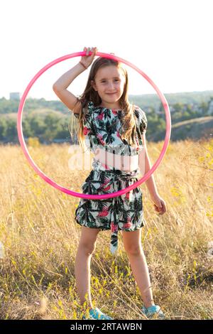 Petite fille avec un cerceau de gymnastique dans la nature en été Banque D'Images