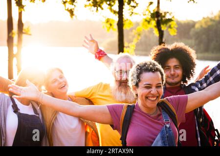 Un groupe de jeunes amis multiraciaux se rassemble près du lac forestier serein, leurs visages rayonnant de bonheur lors d'une escapade estivale. Dans un moment réconfortant, une jeune brésilienne vivante se tient au premier plan, les bras grands ouverts, symbolisant l’unité et la joie partagées entre les divers groupes. Derrière elle, ses amis tout aussi ravis se joignent à la célébration de l’amitié et de la beauté de la nature. Summer Joy par The Lakeside : Multiracial Friends Unite. Photo de haute qualité Banque D'Images