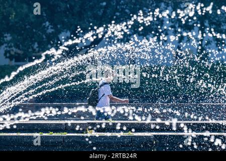Landshut, Allemagne. 12 septembre 2023. Un passant passe derrière une fontaine par temps ensoleillé. Crédit : Armin Weigel/dpa/Alamy Live News Banque D'Images