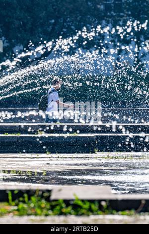 Landshut, Allemagne. 12 septembre 2023. Un passant passe derrière une fontaine par temps ensoleillé. Crédit : Armin Weigel/dpa/Alamy Live News Banque D'Images