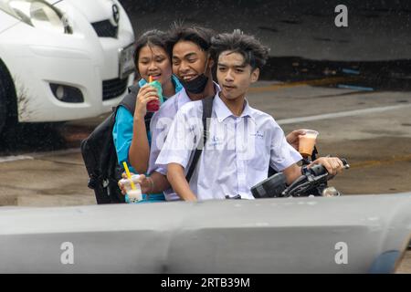 SAMUT PRAKAN, THAÏLANDE, JUIN 06 2023, Un trio d'adolescents joyeux roulent une moto sous la pluie Banque D'Images