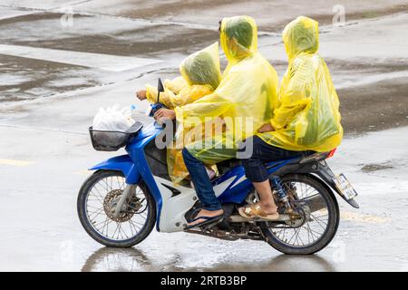 Une famille vêtue d'imperméables conduit une moto sous la pluie, en Thaïlande Banque D'Images