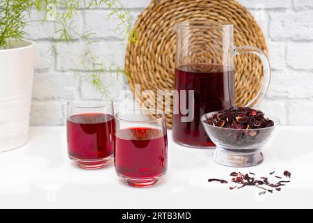 Carafe pleine de thé de fleur d'hibiscus séché, sur table en bois blanc. Banque D'Images