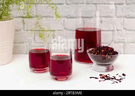 Carafe pleine de thé de fleur d'hibiscus séché, sur table en bois blanc. Banque D'Images