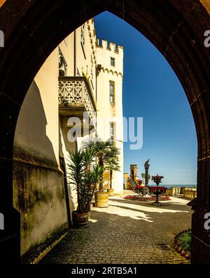 Château de Stolzenfels, vue à travers un portail de style néo-gothique sur la terrasse du Rhin avec palais, colonne d'aigle, palmiers et décorations de pétunia, Kobl Banque D'Images