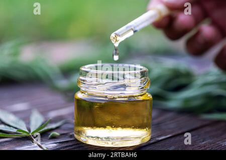 De l'huile jaune s'écoule d'une pipette dans un flacon en verre. Huile cosmétique. Une goutte d'huile de chanvre. Compte-gouttes avec gros plan d'huile. Banque D'Images