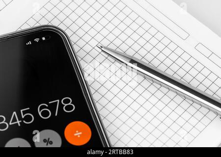 Calculatrice dans le téléphone avec stylo sur ordinateur portable. Table de bureau avec fournitures. Banque D'Images