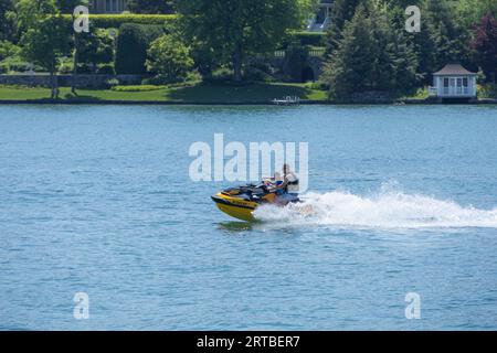 Père et fils sur un jet ski sur le lac Skaneateles dans l'État de New York. Journée d'été ensoleillée avec rivage en vue. Banque D'Images