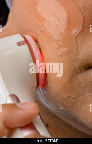 image verticale en gros plan d'une femme méconnaissable nettoyant la peau de son visage avec des ultrasons Banque D'Images