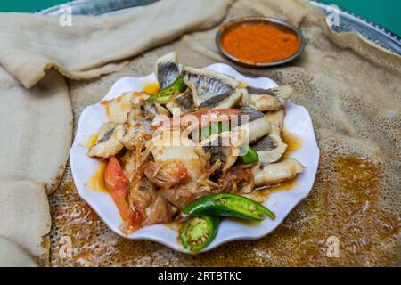 Repas en Ethiopie - morceaux de poisson avec des piments et des légumes sur du pain plat injera Banque D'Images