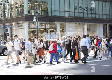 Touristes et New-Yorkais traversent la 5e Avenue le long de la 42e rue par une chaude journée d'été dans le centre de Manhattan. Banque D'Images