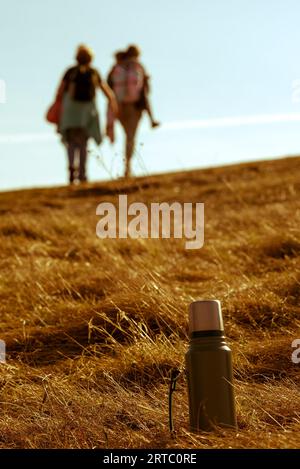 Thermos dans une herbe jaune contre la famille de marche défocalisée Banque D'Images