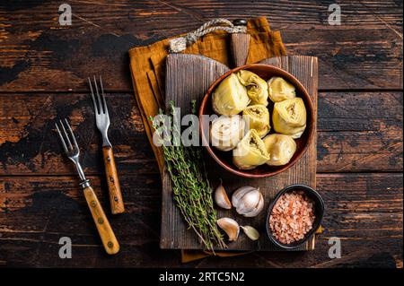 Hors-d'œuvre cœurs d'artichaut marinés dans de l'huile d'olive avec des herbes et des épices fond en bois. Vue de dessus. Banque D'Images