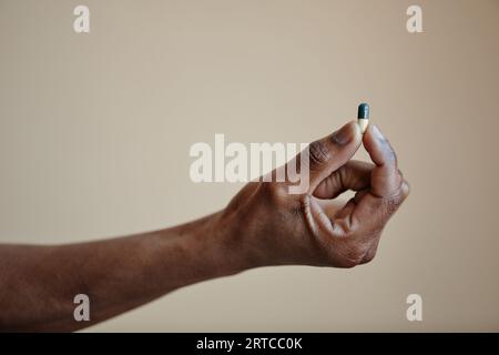 Gros plan de la main masculine noire tenant la pilule de capsule unique sur fond neutre, espace de copie Banque D'Images