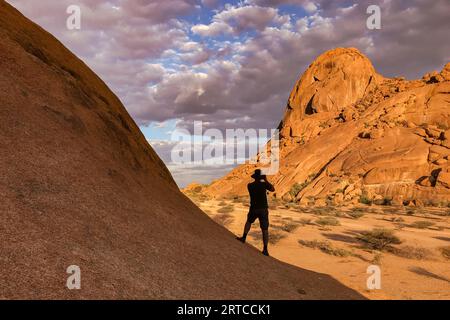 Silhouette d'un photographe prenant une photo des rochers du massif du Spitzkoppe au coucher du soleil, Namibie, Afrique Banque D'Images