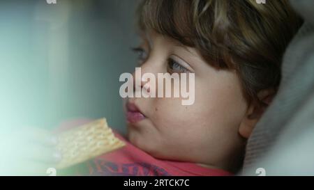 Gros plan visage de petit garçon grignotant cookie, enfant mangeant une friandise sucrée pour la collation Banque D'Images