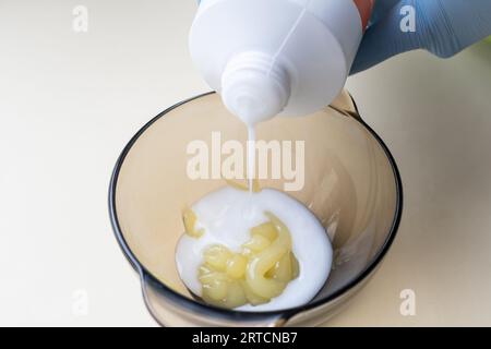 fille dans des gants de protection en caoutchouc bleu tenant une brosse dans ses mains et remuant colorant capillaire gros plan coloriste soins capillaires au masque capillaire à la maison. Banque D'Images