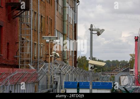 fil de fer barbelé et caméras de surveillance au-dessus de la clôture dans la ville près du mur de construction de briques rouges le jour d'été Banque D'Images