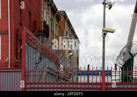 fil de fer barbelé et caméras de surveillance au-dessus de la clôture dans la ville près du mur de construction de briques rouges le jour d'été Banque D'Images