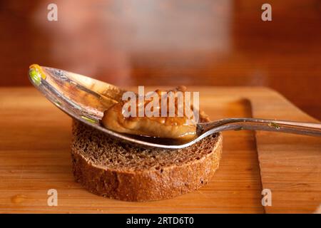 Champignon brun de forêt mariné se trouve dans une cuillère sur un morceau de pain noir sur une planche, déjeuner, champignons pour le déjeuner sur la table Banque D'Images