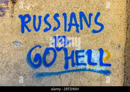 Les mots "Les Russes vont en Enfer" sont peints en bleu sur un mur d’une maison de la rue Arsena Odzelashvili dans le quartier Mtatsminda de Tbilissi, en Géorgie. Un trait bleu souligne les mots. Des taches de peinture blanches et jaunes se trouvent derrière les lettres "LL". En 2023, des graffitis contre la Russie et en faveur de liens plus étroits avec l’Europe ont façonné le paysage urbain de la capitale. Banque D'Images