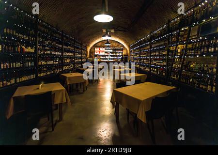 La cave à vin Sazvele avec tables et chaises. Des étagères avec des bouteilles de vin bordent les murs. Au bout de la salle se trouve un bar. La scène se déroule à Tbilissi, en Géorgie. Sazvele offre une atmosphère confortable et authentique, parfaite pour déguster du vin géorgien Banque D'Images
