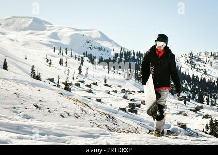 homme marchant sur une colline avec des montagnes de surf des neiges en arrière-plan Banque D'Images