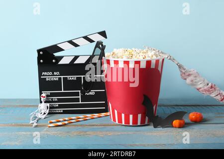 Clapperboard de film et seau de pop-corn avec décor d'Halloween sur la table en bois sur fond bleu Banque D'Images