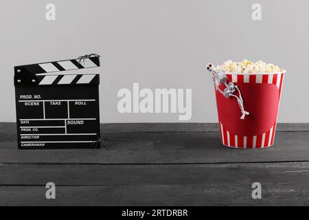 Seau avec pop-corn, squelette et clapperboard de film sur table en bois sur fond gris Banque D'Images