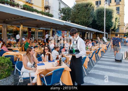 Un serveur servant les clients assis au bar et restaurant Fauno situé sur la place Piazza Tasso, Sorrente, Italie. Sorrente est une ville côtière du sud-ouest de l'Italie, face à la baie de Naples sur la péninsule de Sorrente. Perché au sommet des falaises qui séparent la ville de ses ports de plaisance animés, il est connu pour ses vues panoramiques sur l'eau et la Piazza Tasso, une place bordée de cafés. Banque D'Images