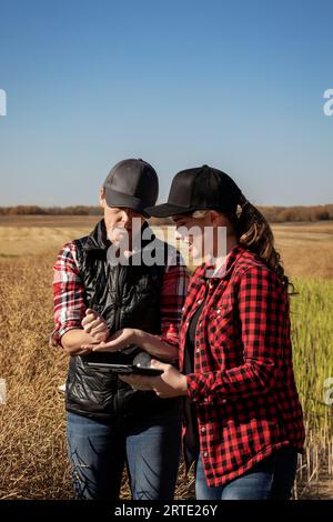 Une agricultrice debout dans les champs enseignant à son apprenti les techniques agricoles modernes pour les cultures de canola en utilisant les technologies sans fil et... Banque D'Images