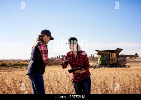 Une femme agricole mature debout dans un champ travaillant avec une jeune femme à la récolte inspectant le grain et utilisant un logiciel agricole avancé sur... Banque D'Images