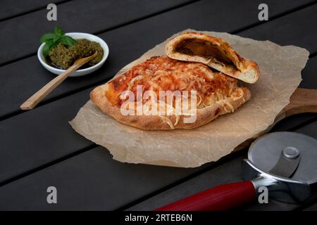 Pizza calzone découpée avec sauce tomate, pesto vert et fromage sur assiette en bois Banque D'Images