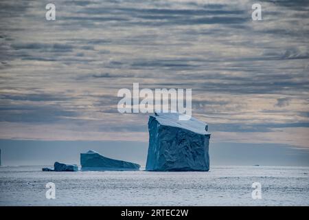 Icebergs massifs flottant dans la zone du détroit antarctique du Groenland avec un ciel nuageux spectaculaire ; est du Groenland, Groenland Banque D'Images