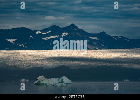 Soleil de fin de journée sur le glacier du fjord de Nansen avec la silhouette des pics de montagne déchiquetés en arrière-plan sous un ciel bleu-gris nuageux Banque D'Images