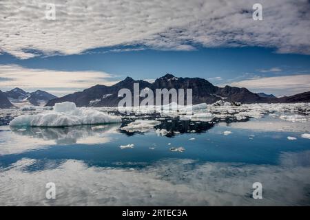 Pics de montagne dentelés et nuages blancs reflétés dans les eaux calmes du fjord de Nansen avec des icebergs et des growlers flottant au premier plan au... Banque D'Images