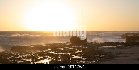 Une photo anti-lumière de minuscules gouttelettes de vagues de mer heurtant un brise-lames au coucher du soleil. Banque D'Images