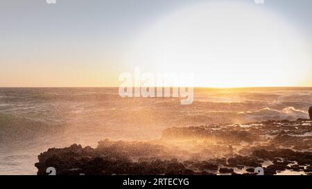 Une photo anti-lumière de minuscules gouttelettes de vagues de mer heurtant un brise-lames au coucher du soleil. Banque D'Images