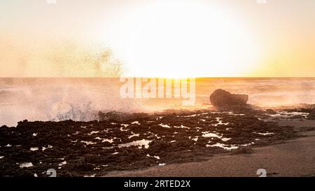 Une photo anti-lumière de minuscules gouttelettes de vagues de mer heurtant un brise-lames au coucher du soleil. Banque D'Images