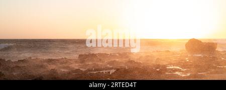 Une photo anti-lumière de minuscules gouttelettes de vagues de mer heurtant un brise-lames au coucher du soleil. Banque D'Images