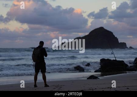 Vue de derrière d'un homme en silhouette debout sur la plage regardant l'océan Pacifique au crépuscule sur la route de Hana Banque D'Images