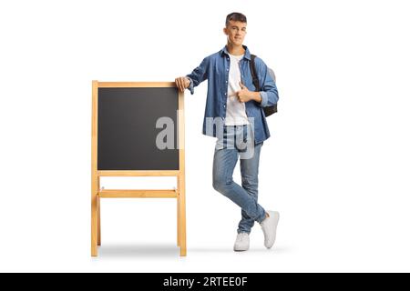 Étudiant adolescent masculin avec un sac à dos pointant vers un petit tableau noir isolé sur fond blanc Banque D'Images