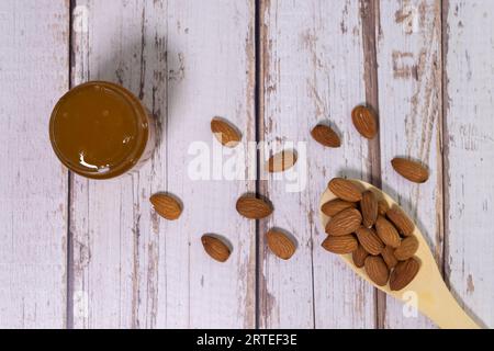 Forme de coeur composée de différentes graines d'amandes à côté de la cuillère en bois sur le fond blanc isolé Banque D'Images