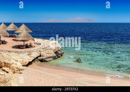 Station balnéaire ensoleillée de corail tropical avec parasols de paille à Charm el Cheikh, Egypte. Banque D'Images