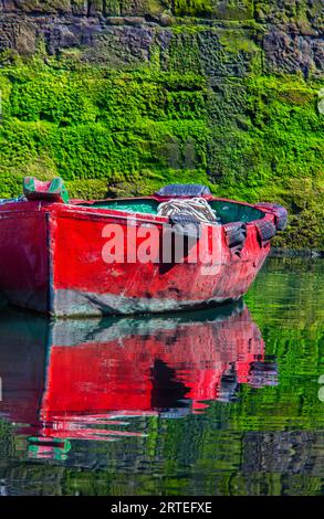 Petit bateau de pêche en bois amarré au rivage avec un reflet d'image miroir dans l'eau calme dans la ville côtière de Getaria Banque D'Images