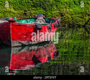 Petit bateau de pêche en bois amarré au rivage avec un reflet d'image miroir dans l'eau calme dans la ville côtière de Getaria Banque D'Images