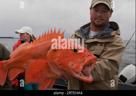 L'homme tient un gros poisson jaune qu'il a pêché au large de l'île Prince of Wales ; Thorne Bay, Alaska, États-Unis d'Amérique Banque D'Images