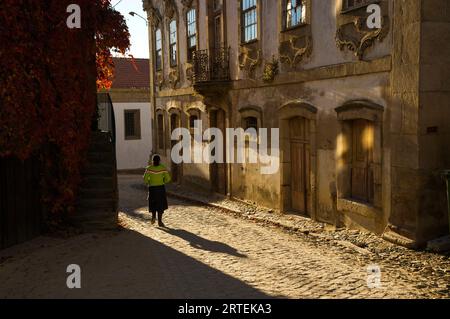 Vue rétroéclairée d'une femme marchant dans une rue pavée dans un village ; Provesende, vallée du fleuve Douro, Portugal Banque D'Images