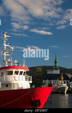 Bateaux amarrés dans le port de Bergen, avec une église bâtie le long du bord de l'eau ; Bergen, Norvège Banque D'Images