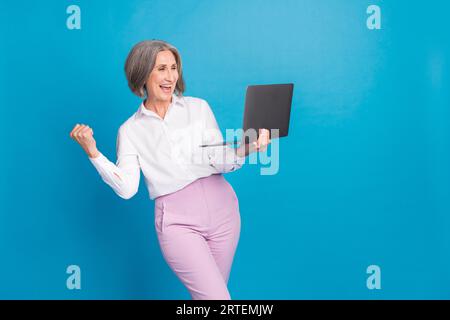 Photo de la femme chanceuse confiante porter chemise blanche gagnant le jeu moderne gadget vide espace isolé fond de couleur bleue Banque D'Images